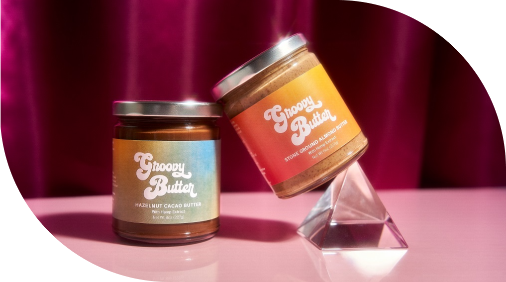 Groovy Butter Hazelnut Cacao Butter with Hemp Extract and Groovy Butter Stone Ground Almond Butter with Hemp Extract are shown balancing on a crystal pyramid. CBD Almond Butter. CBD Nutella. Healthy Vegan Nutella.