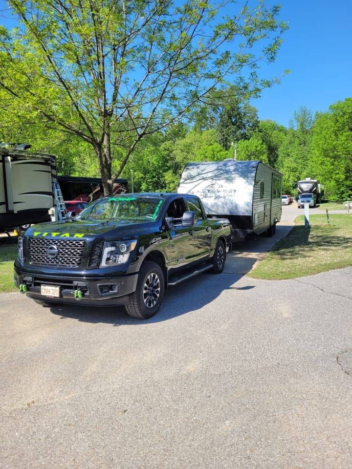 Front three-quarter view of Scott's black 2019 Nissan Titan towing a travel trailer in a campground with HornBlasters Conductor's Special 244K Spare Tire Delete kit featured customer install gallery photo 1
