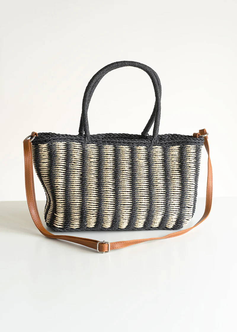 A black and white striped wicker basket with a leather shoulder strap