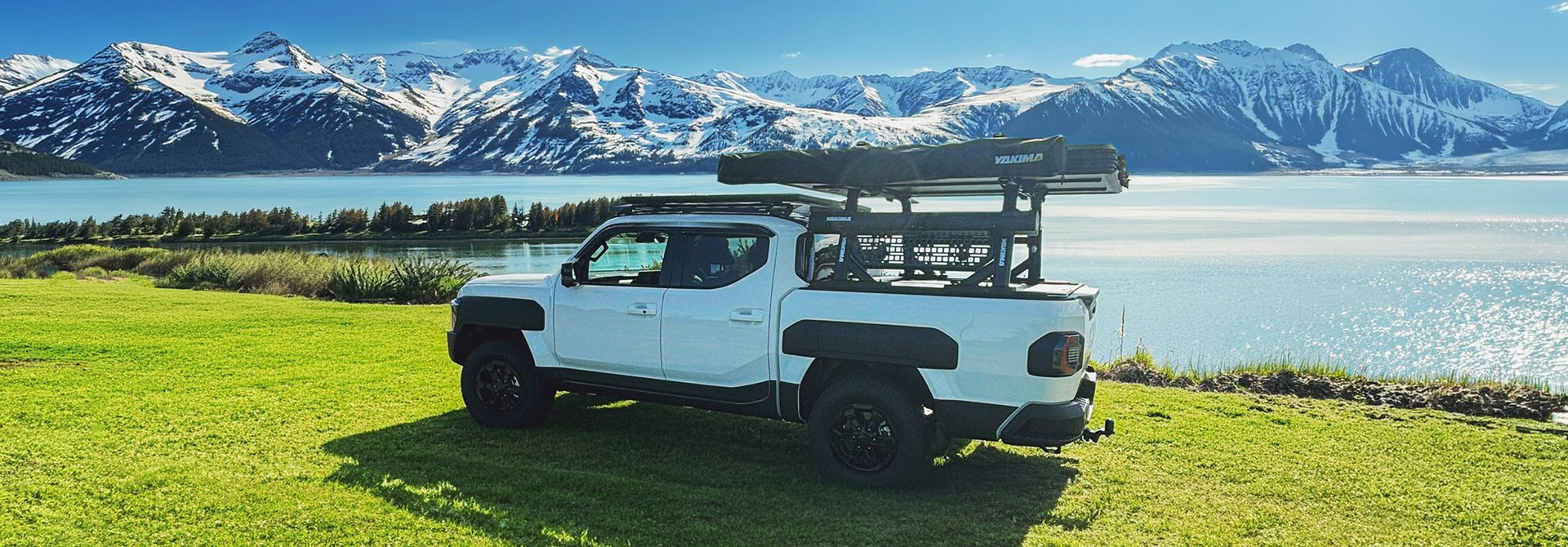 A Kia Tasman Ute with Yakima Accessories in front of a lake and snow capped mountains