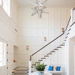 Geometric wall made with white trim over a white wall with a grand staircase.
