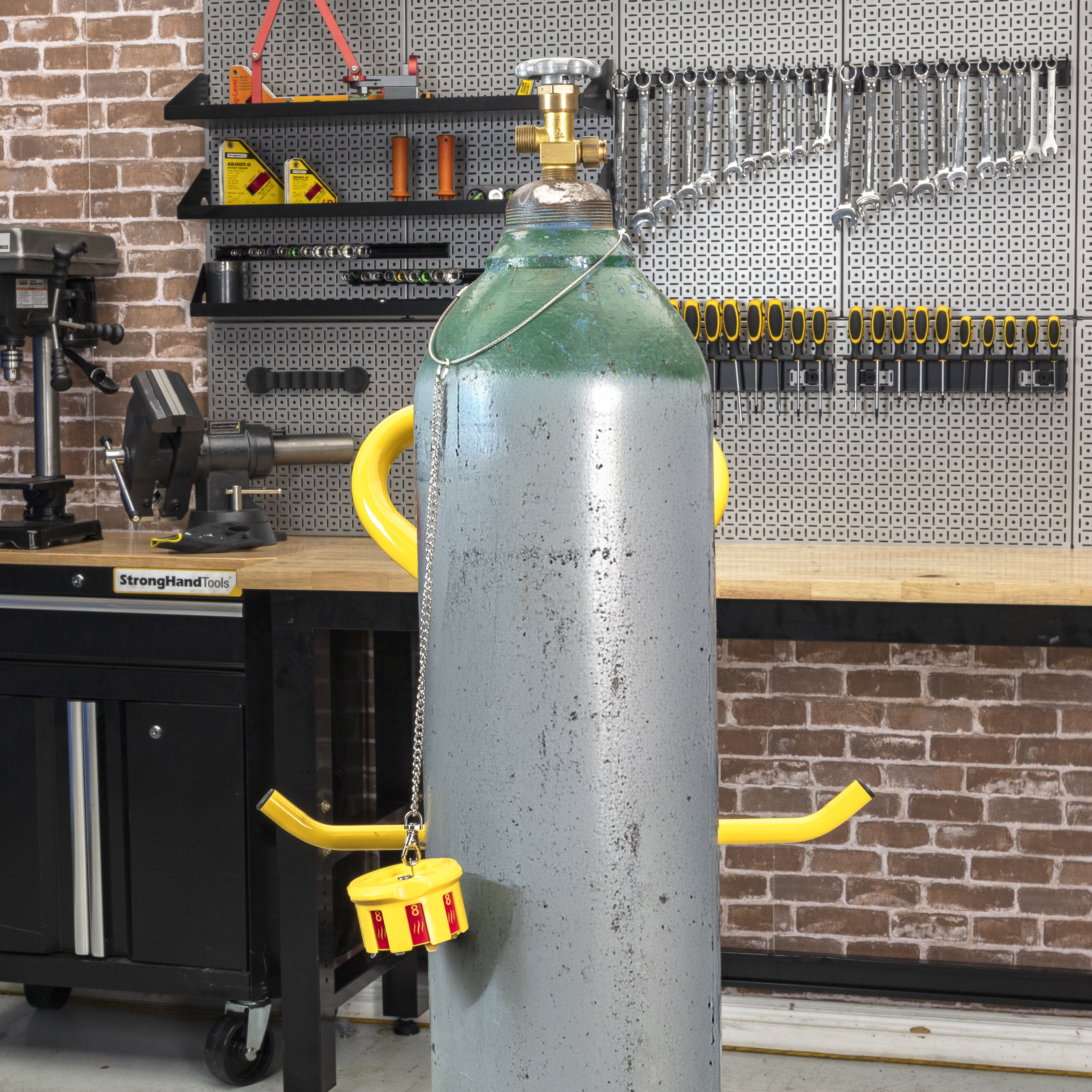 Gray gas cylinder with yellow handles in a workshop setting.