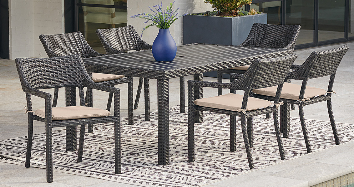 Outdoor dining set with six chairs and a vase on a patterned rug.