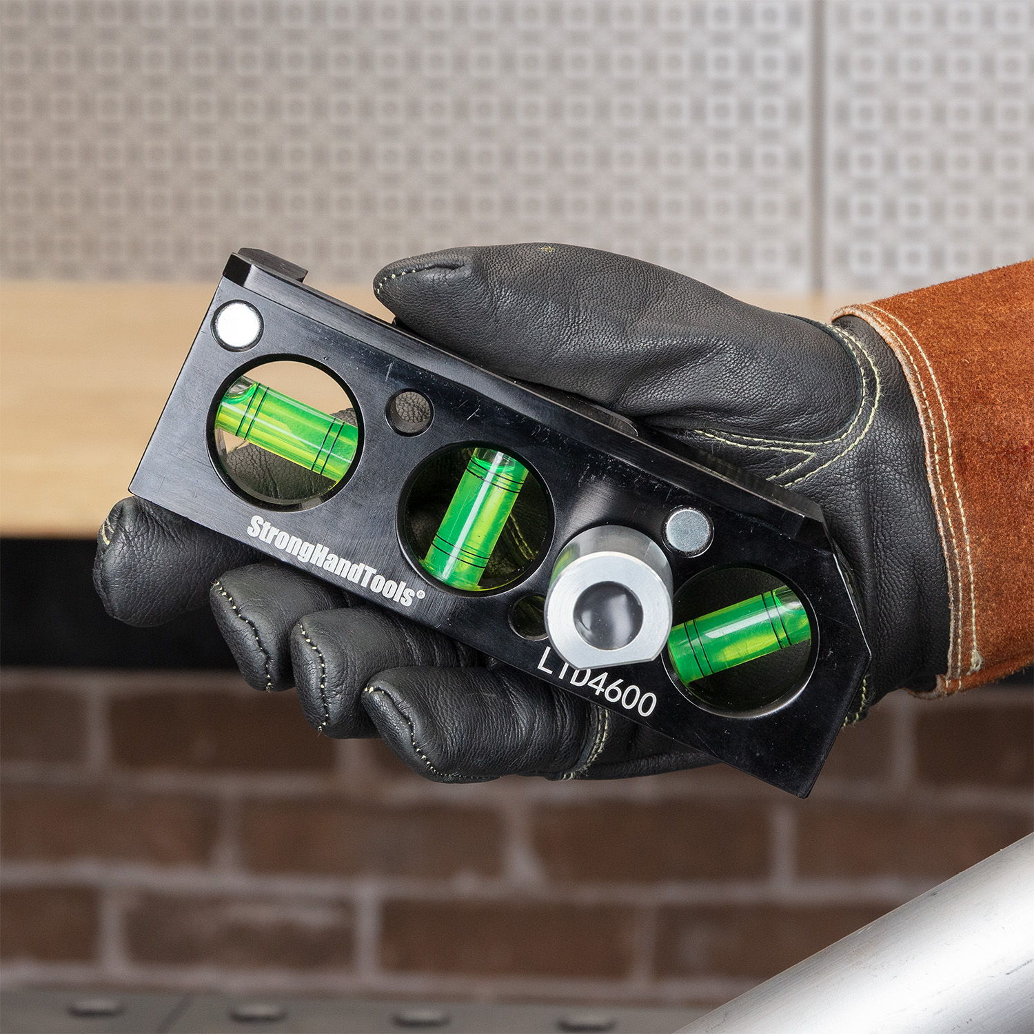 Hand holding a black level tool with green vials.