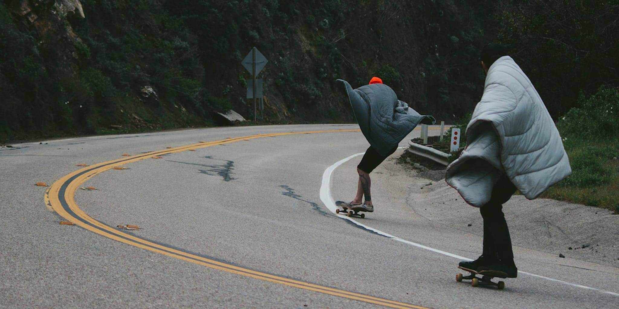 Two guys skateboarding on a road down the hill with Rumpl blankets