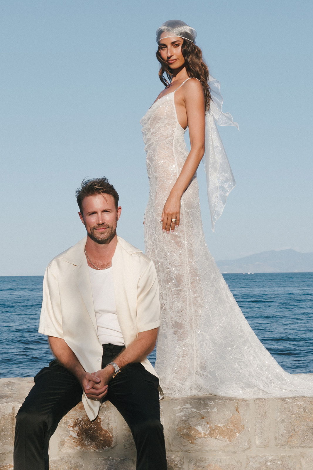 A man and woman in wedding attire by the sea.