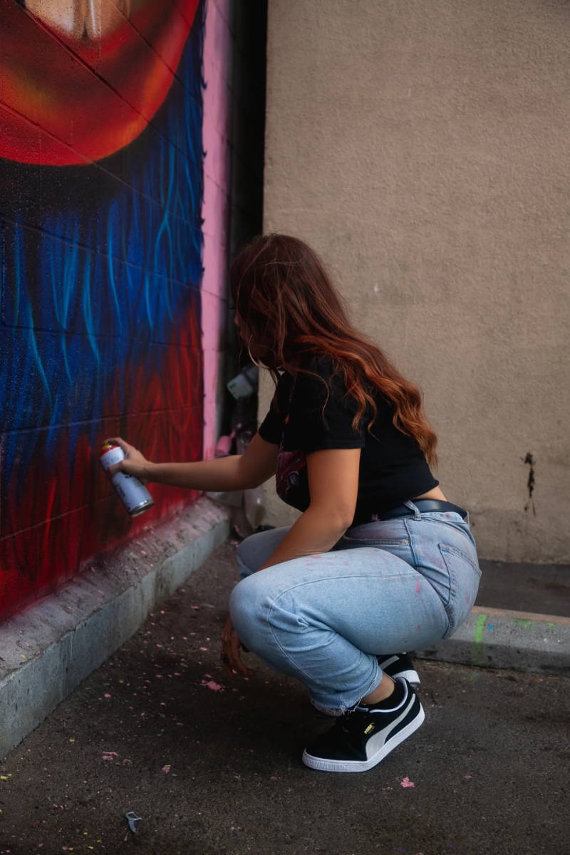 woman spraypainting wall wearing puma suede shoes
