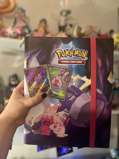 A hand holding the Tinkaton and Tinkaton ex Illustration Rare cards from Paldea Evolved in front of a custom Tinkaton-themed Pokémon TCG binder.