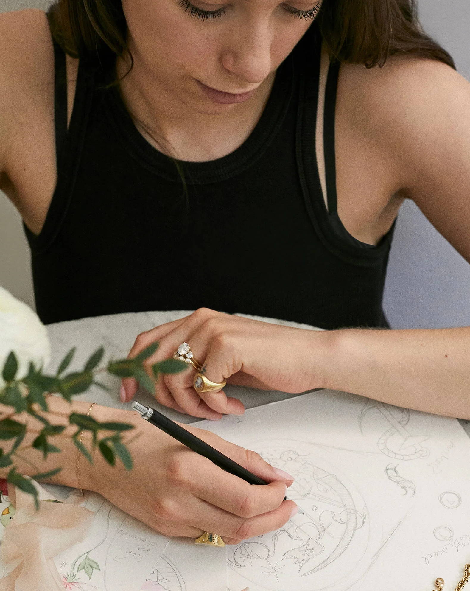 Woman drawing on paper at a table with flowers nearby.