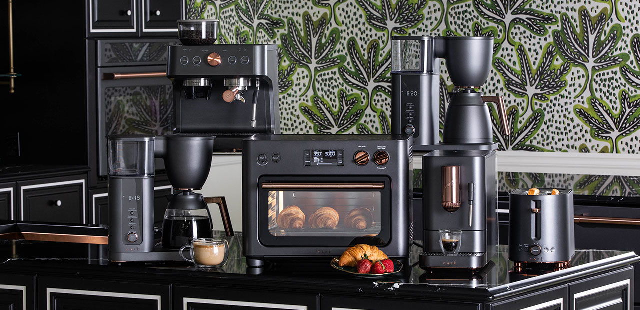 Kitchen countertop with various matte black countertop appliances and decorative wallpaper.