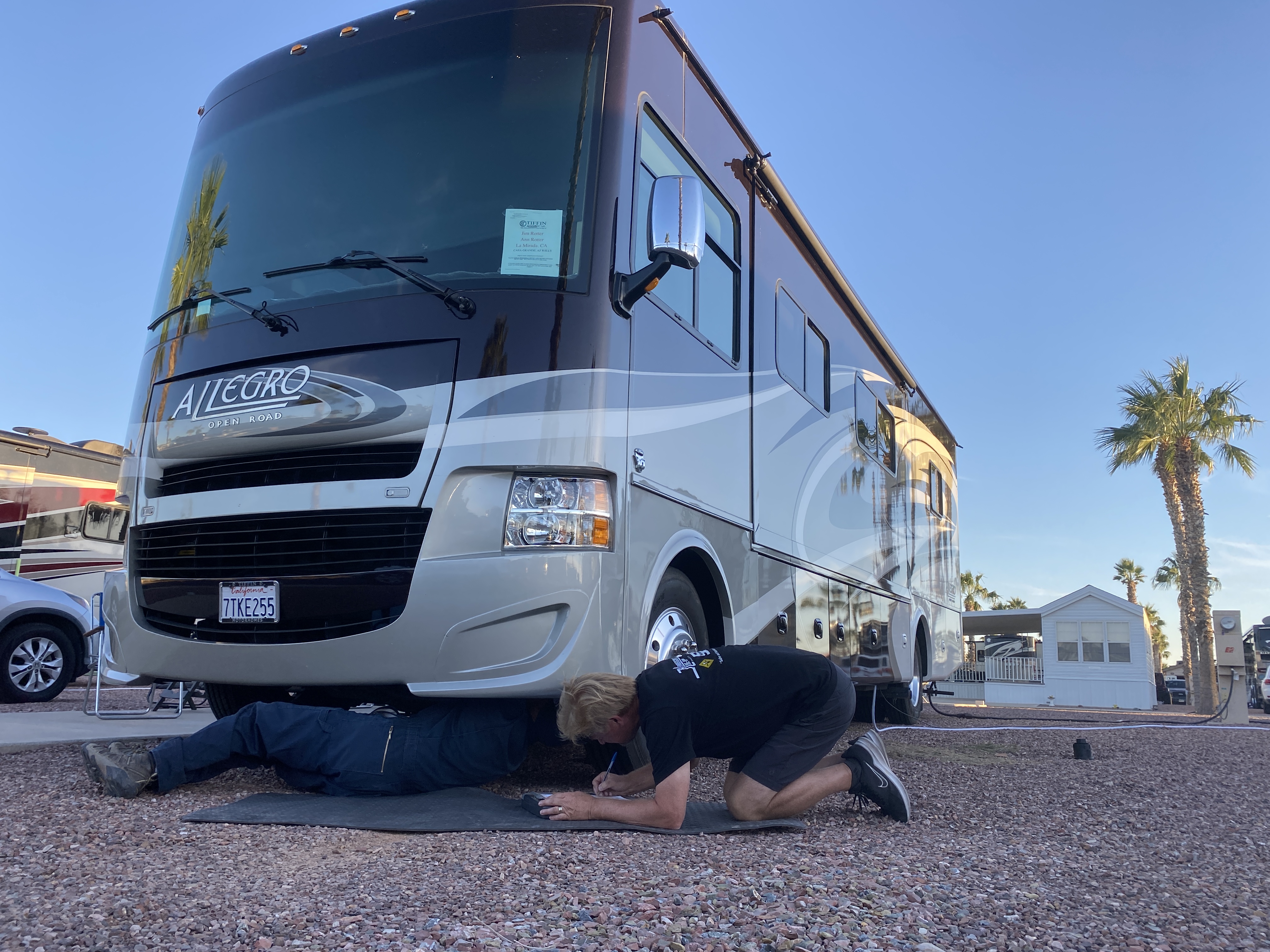 Two people working under an RV in a parking area.