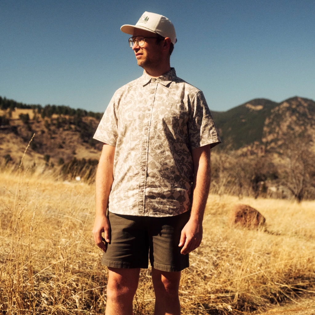 Person standing in a field with mountains in the background, wearing casual clothing.