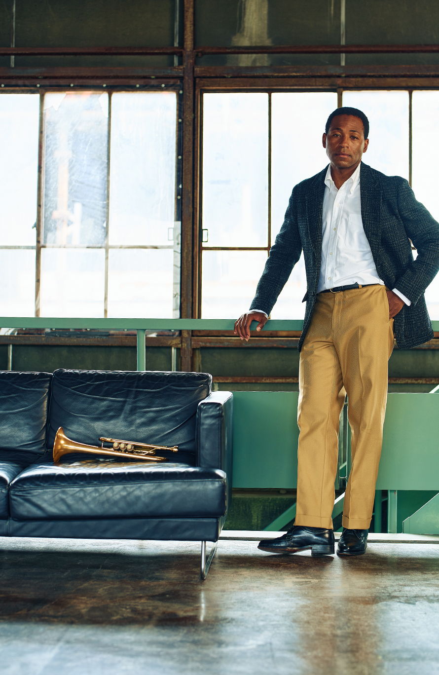 A man stands beside a couch with a trumpet in a room.