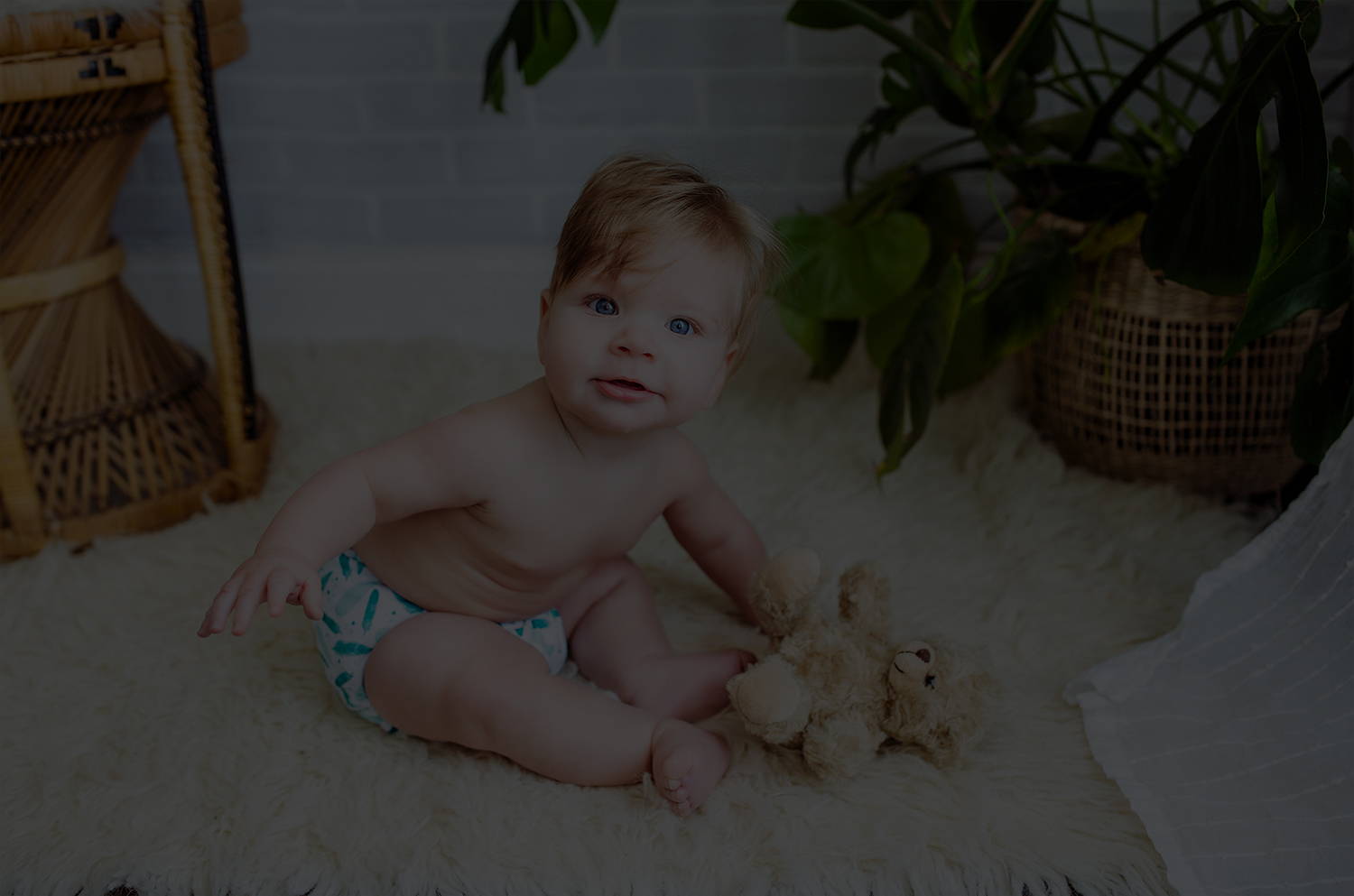 Baby sitting on a cozy fur rug looking right at the camera while holding a stuffed bear. Dressed in his simple being safari.
