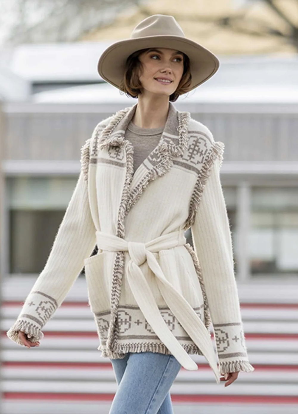 Woman wearing a stylish cream coat and wide-brimmed hat outdoors.