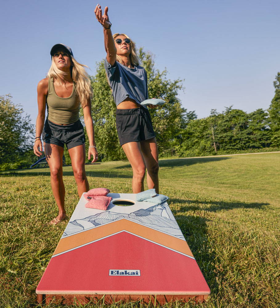 Two girls playing cornhole game outdoors