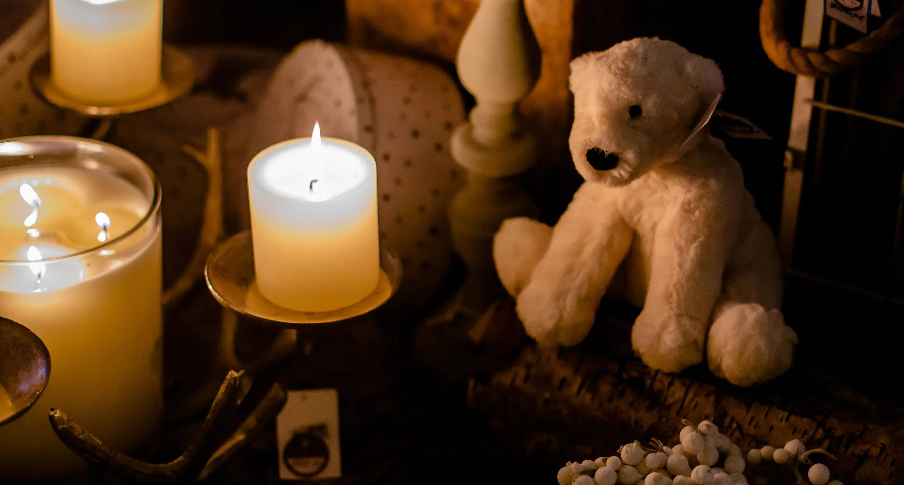 Candle burning next to teddy and Christmas gifts