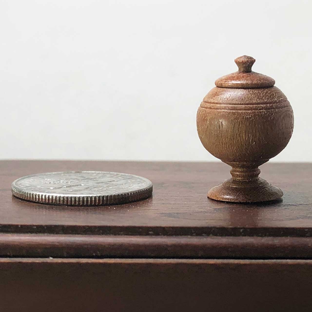 A small wooden globe beside a quarter on a wooden surface.