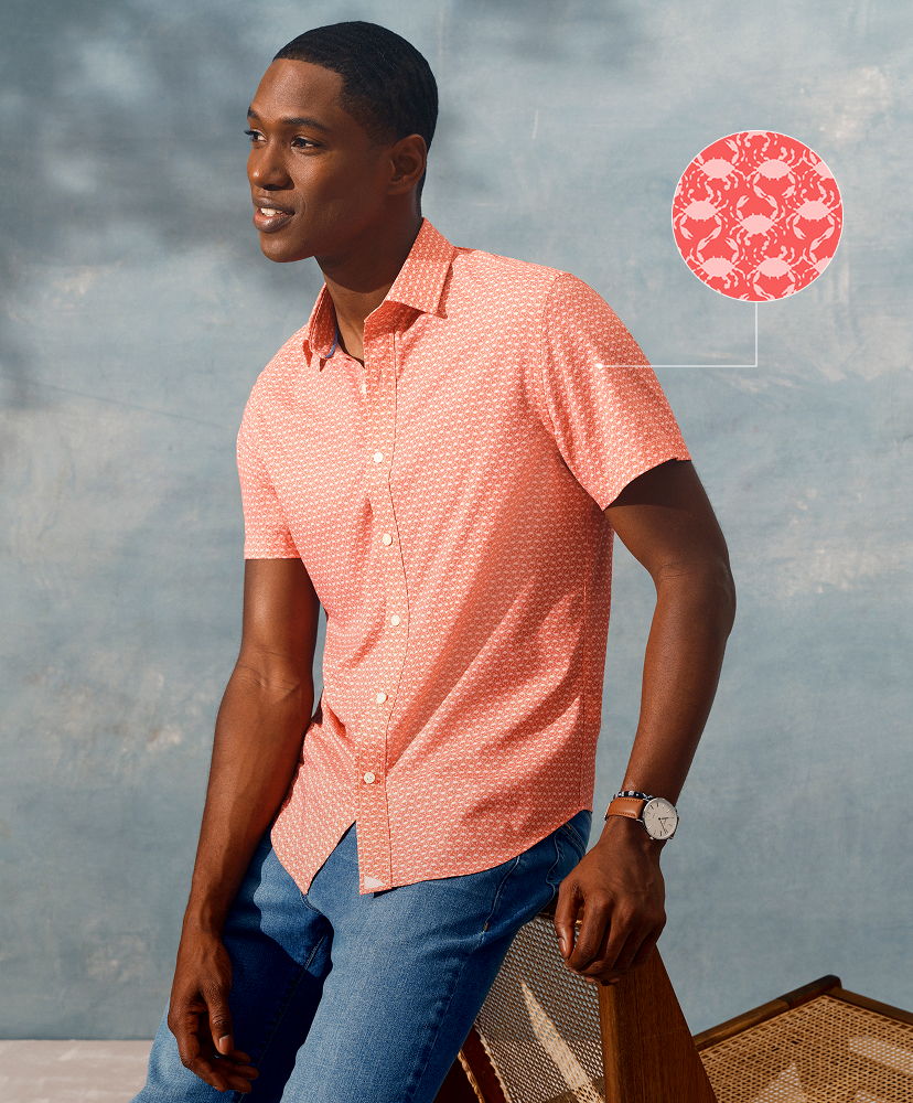 Man in a pink shirt and jeans, posing against a blue background.