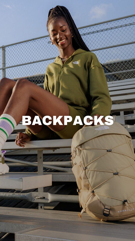 A person sitting on bleachers with a backpack, wearing casual athletic clothing.