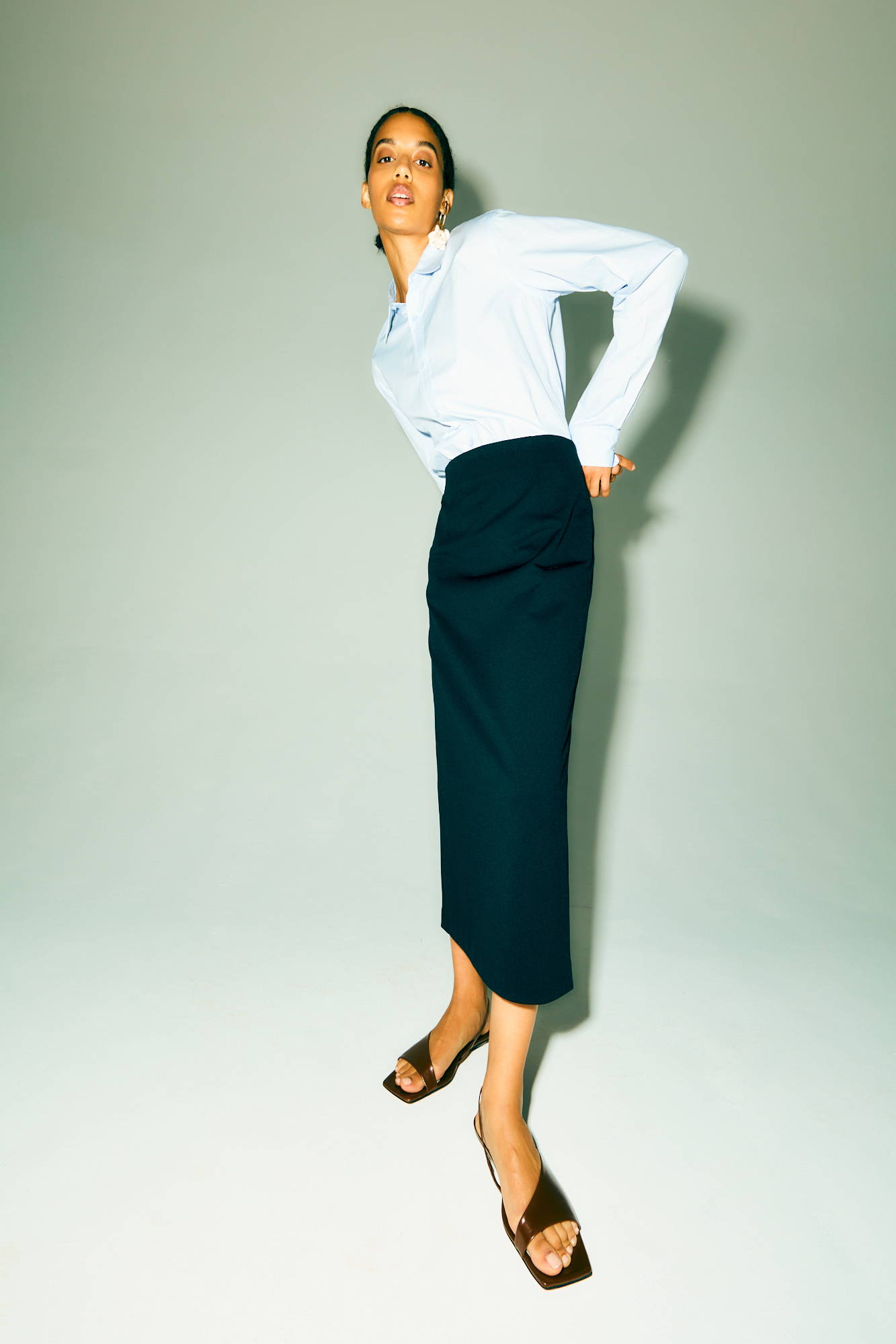 Woman in a white shirt and black skirt posing against a gray background.
