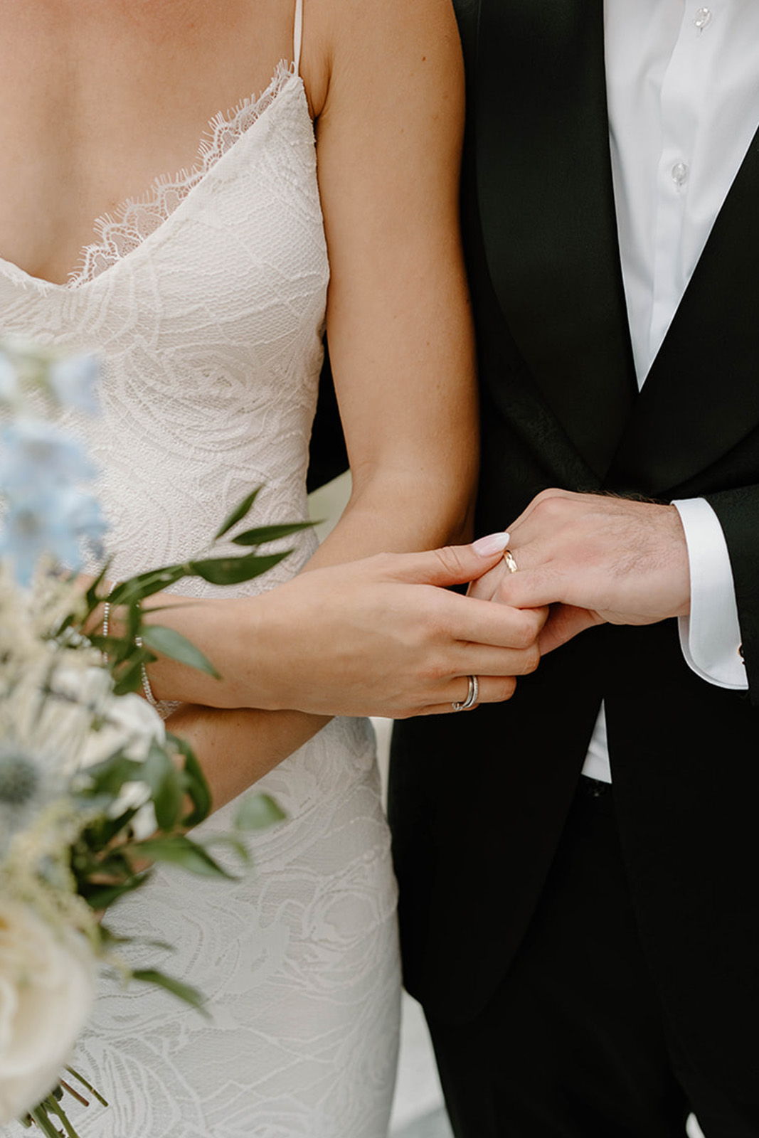 A couple holding hands, showcasing wedding rings and a bouquet.