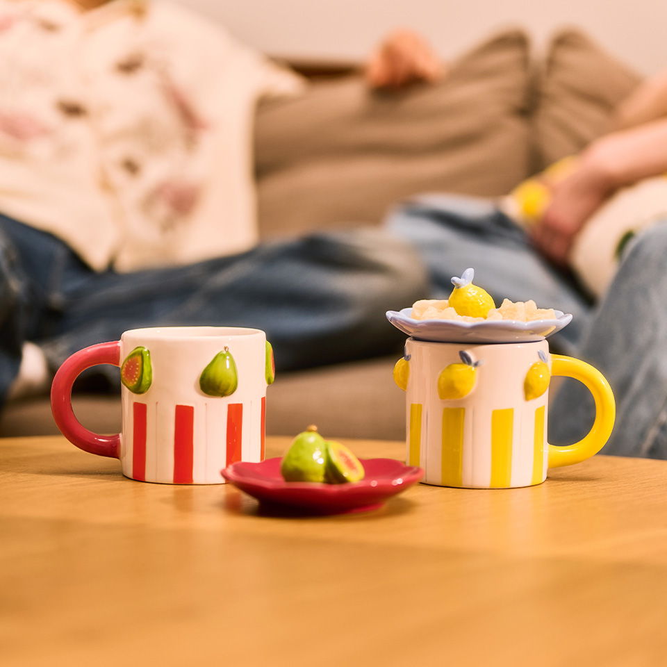 Colorful mugs and a plate with fruits on a wooden table.