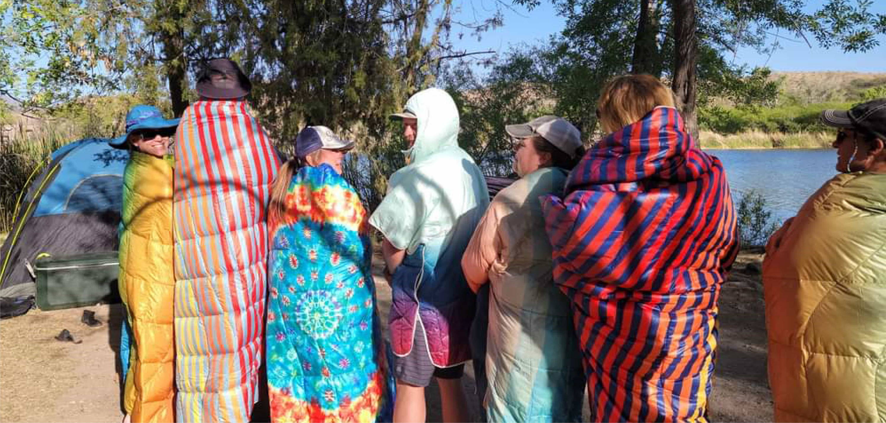 Group Of Men and Womend Wrapped in Rumpl Puffy Blankets On Shore Of River