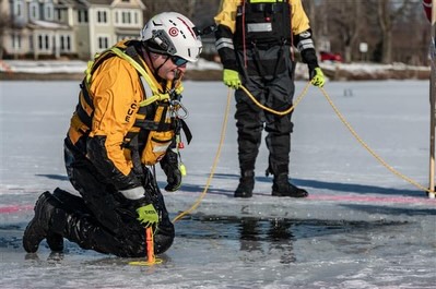 Rescue workers kneeling on ice, testing thickness with a measuring tool.