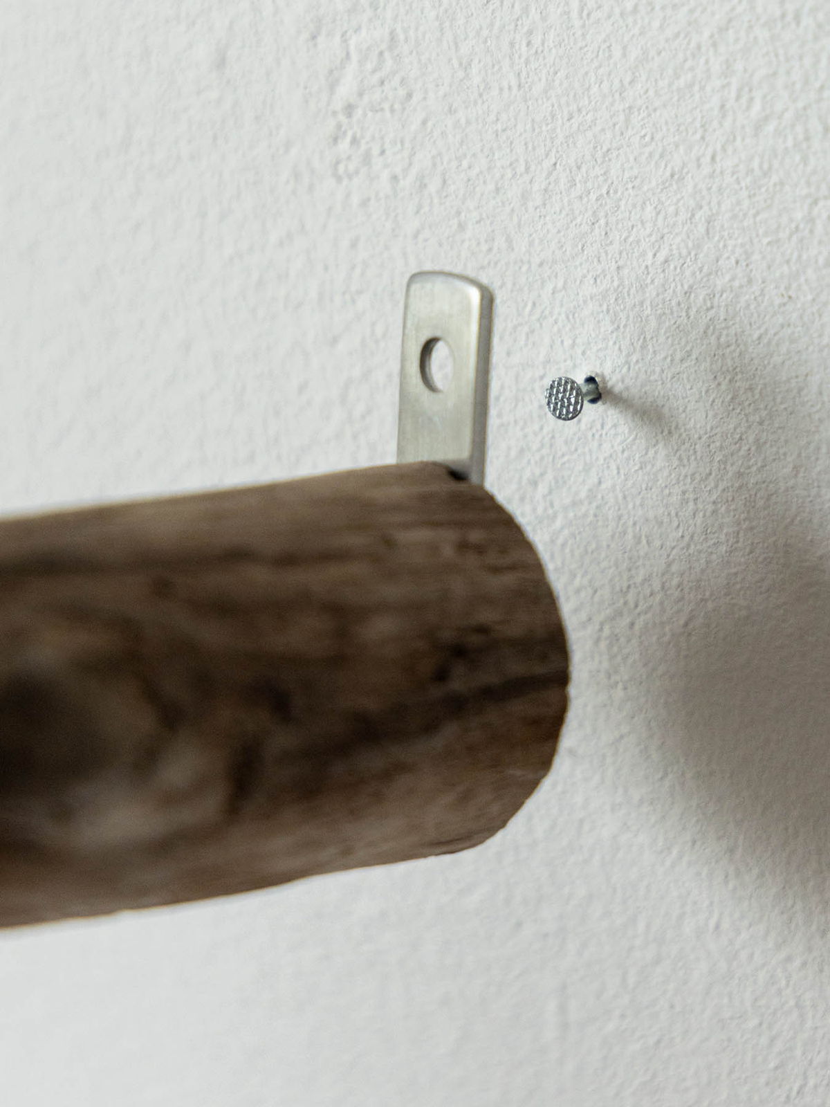 Wooden rod attached to wall with a metal bracket and a screw.