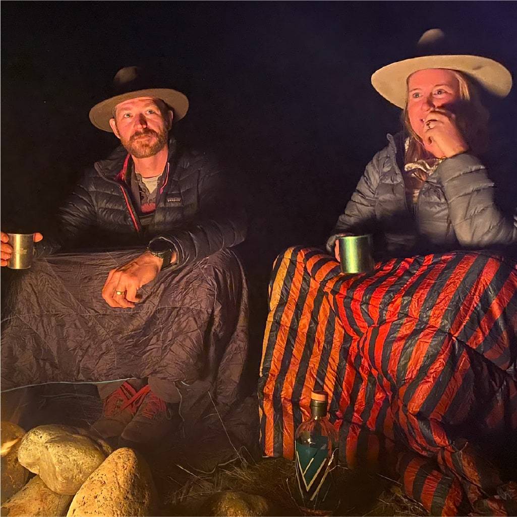 Two people sitting with rumpl blankets around the fire
