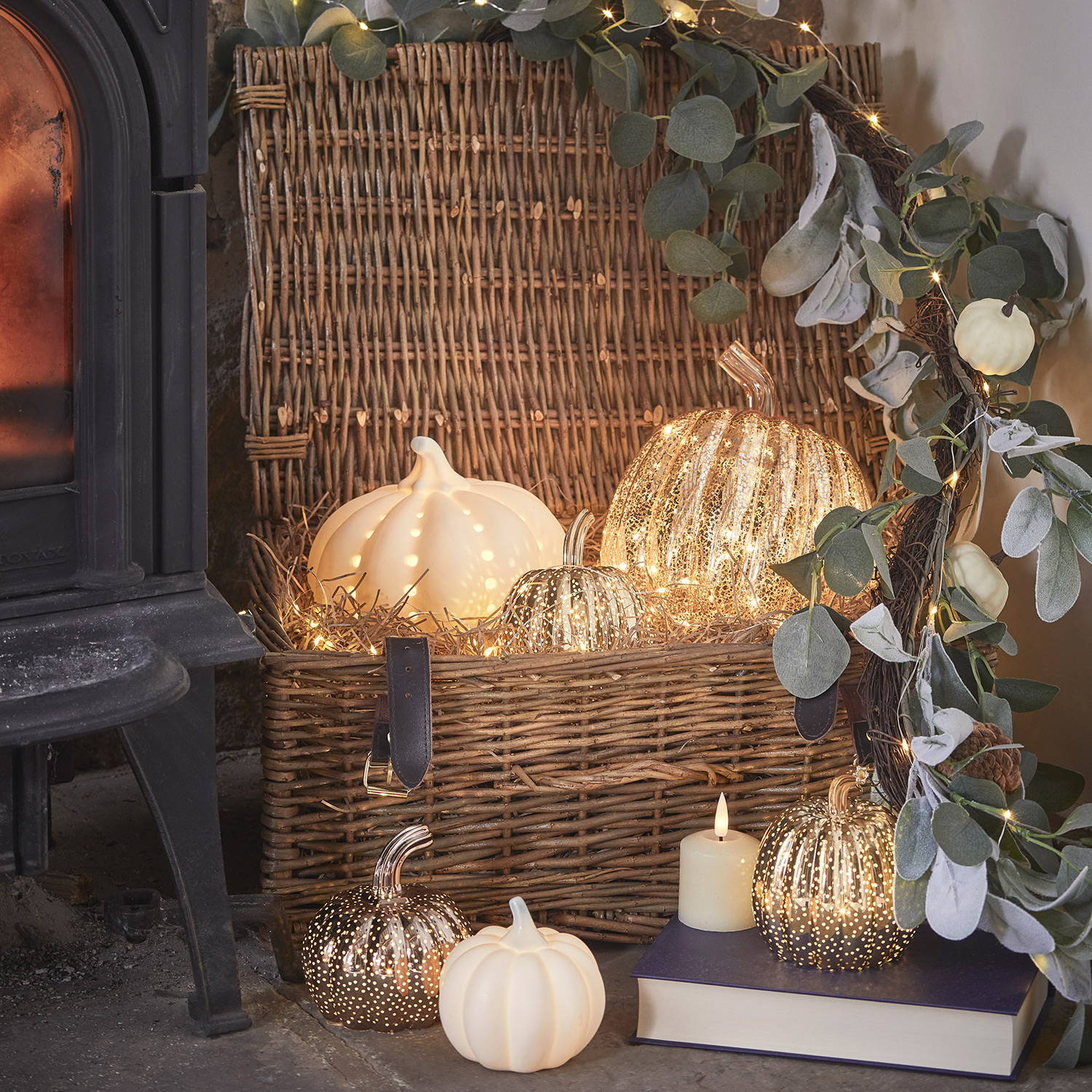 A wicker hamper filled with light up pumpkins and micro lights with additional pumpkins on the floor and an autumn garland around.