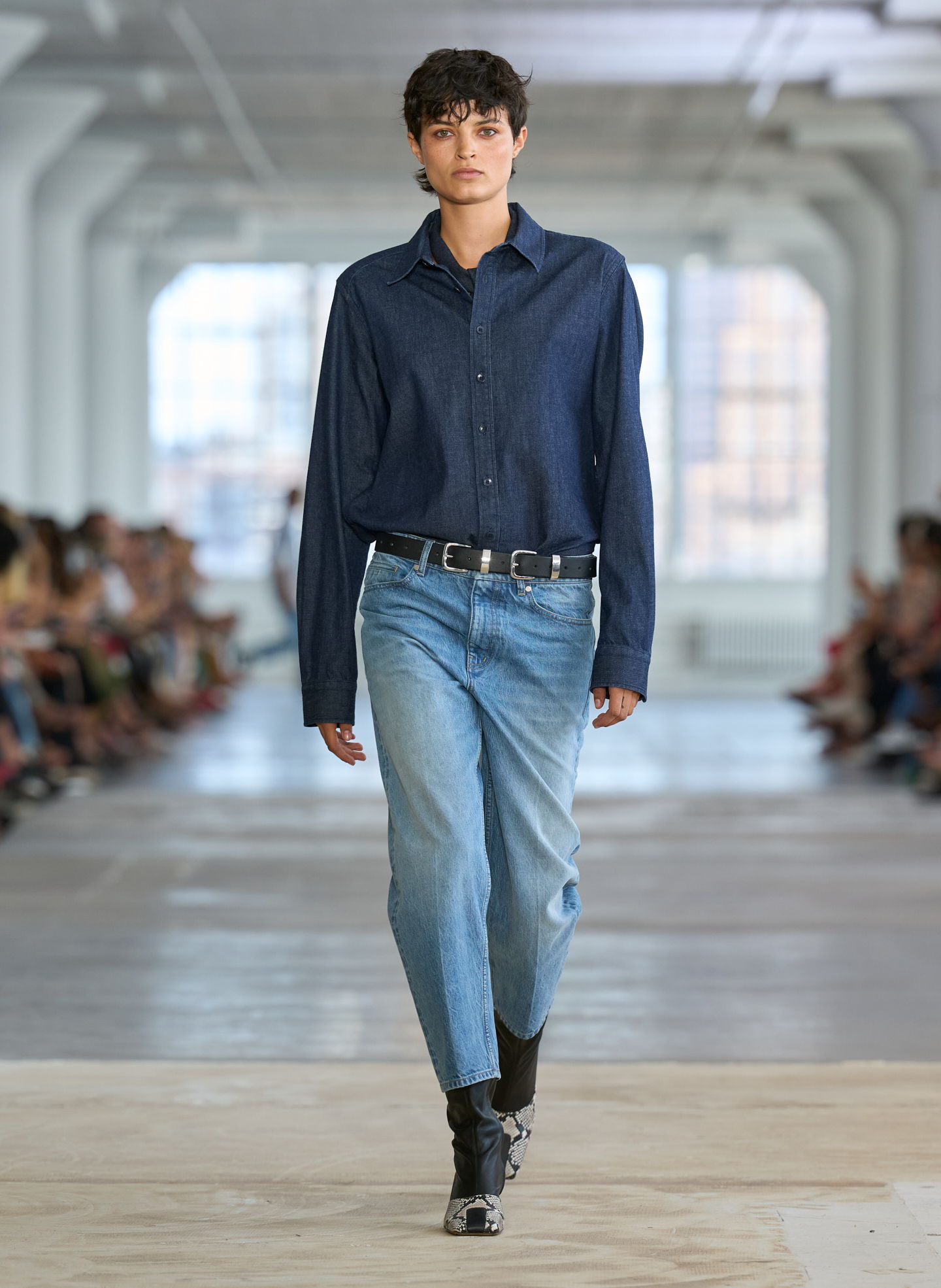 A model walks down the runway in casual attire during a fashion show.
