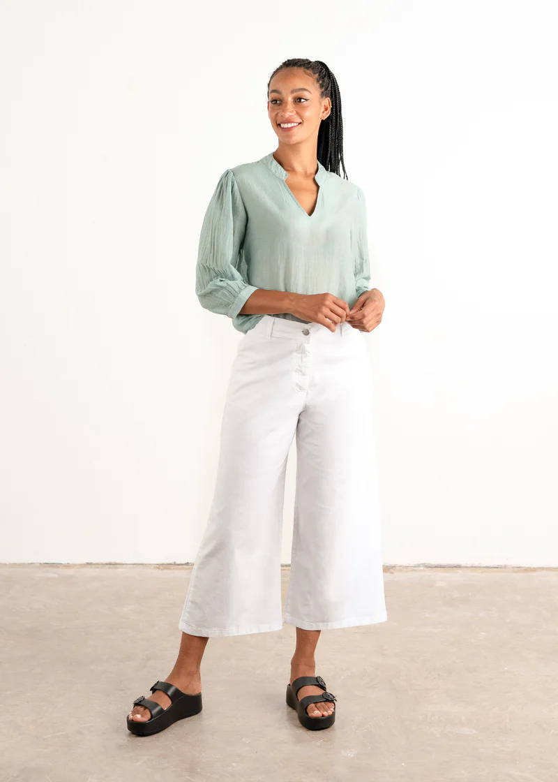 A model wearing an aqua blue long sleeved blouse with white, wide leg trousers and black chunky slides