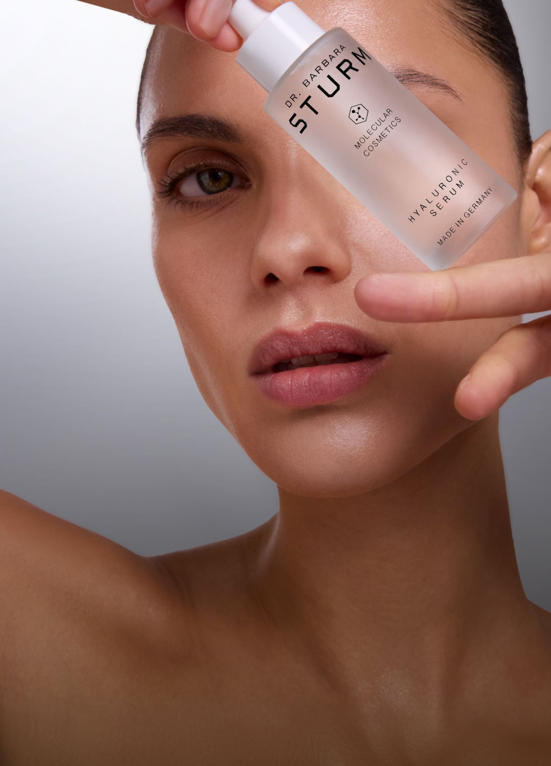 Woman holding a skincare serum bottle near her face.