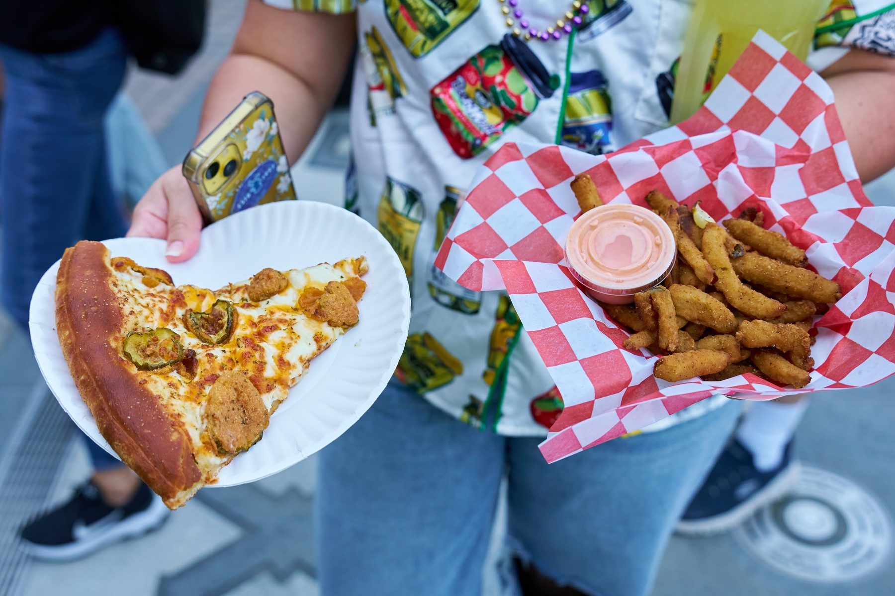 Guest holding pickle pizza slice and fried pickles with dipping sauce at The Big Dill pickle festival.