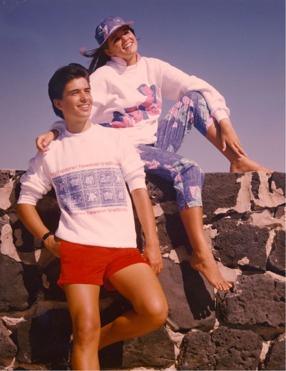 Two young adults posing on a wall, wearing casual summer outfits.