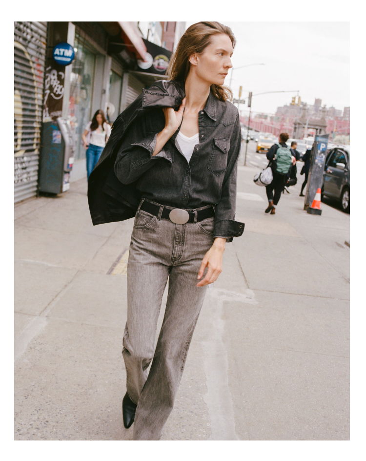 Woman walking on the sidewalk, wearing a black jacket and gray pants.