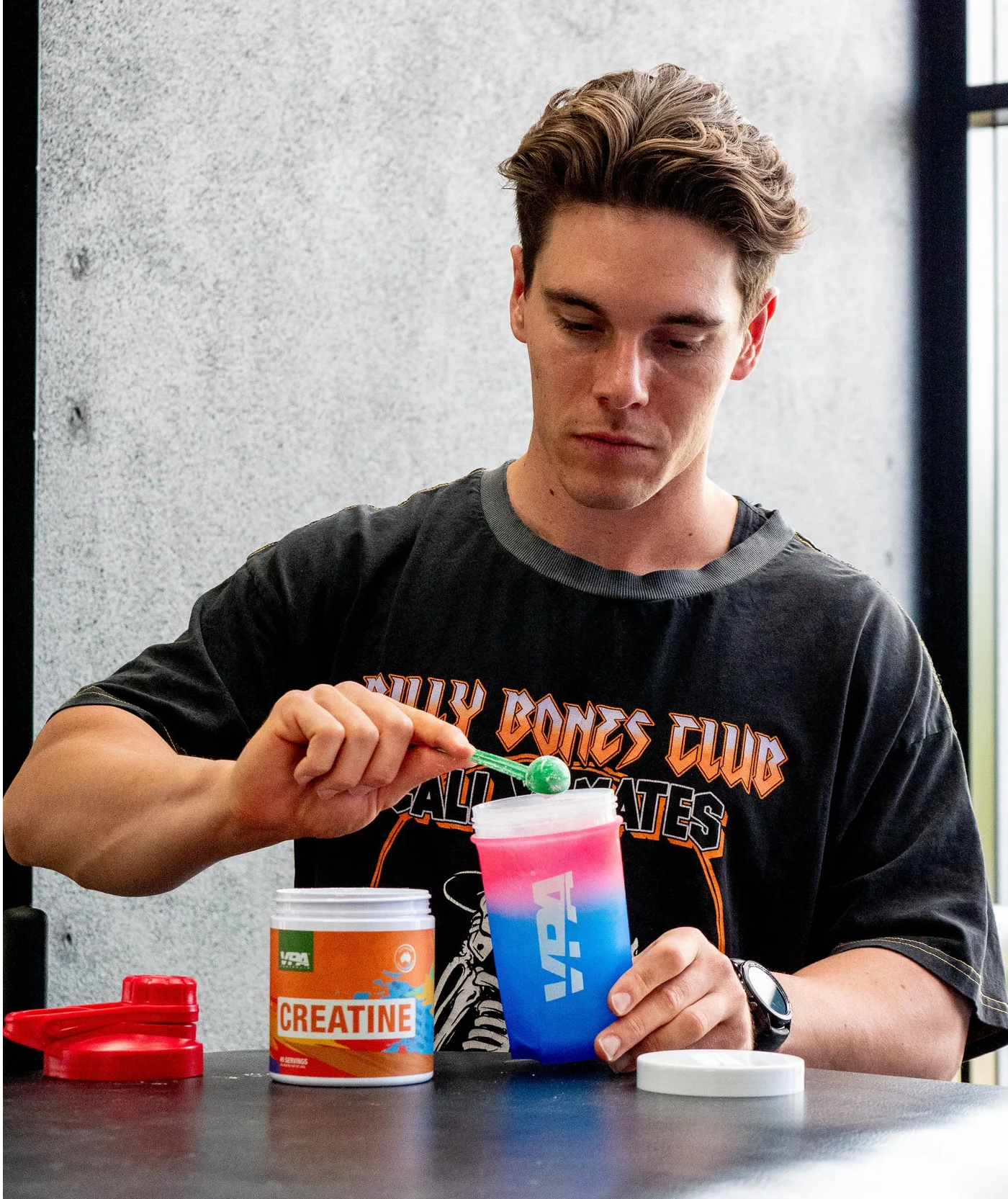 Man mixing creatine powder in a blue shaker bottle at a table.