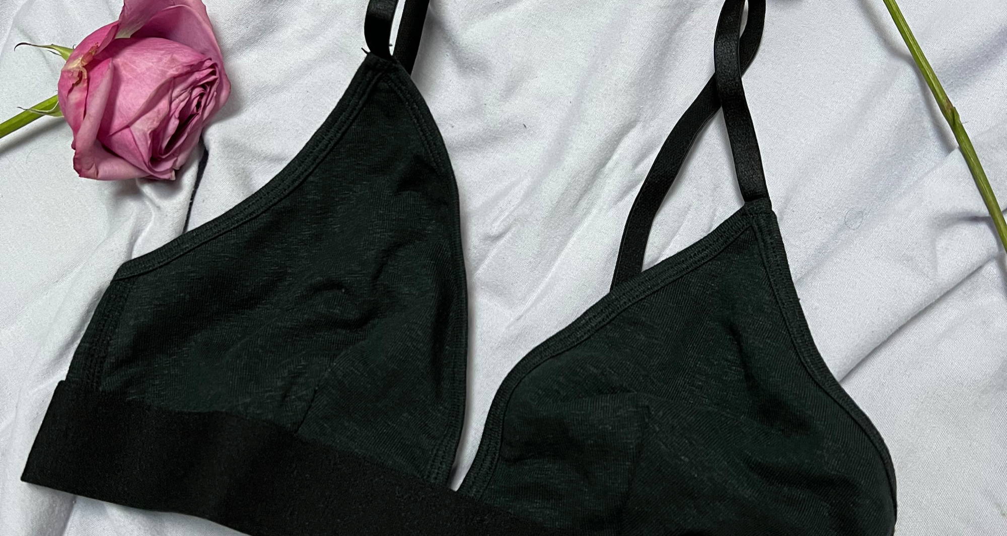 black triangle bralette lays next to dried rose on white comforter