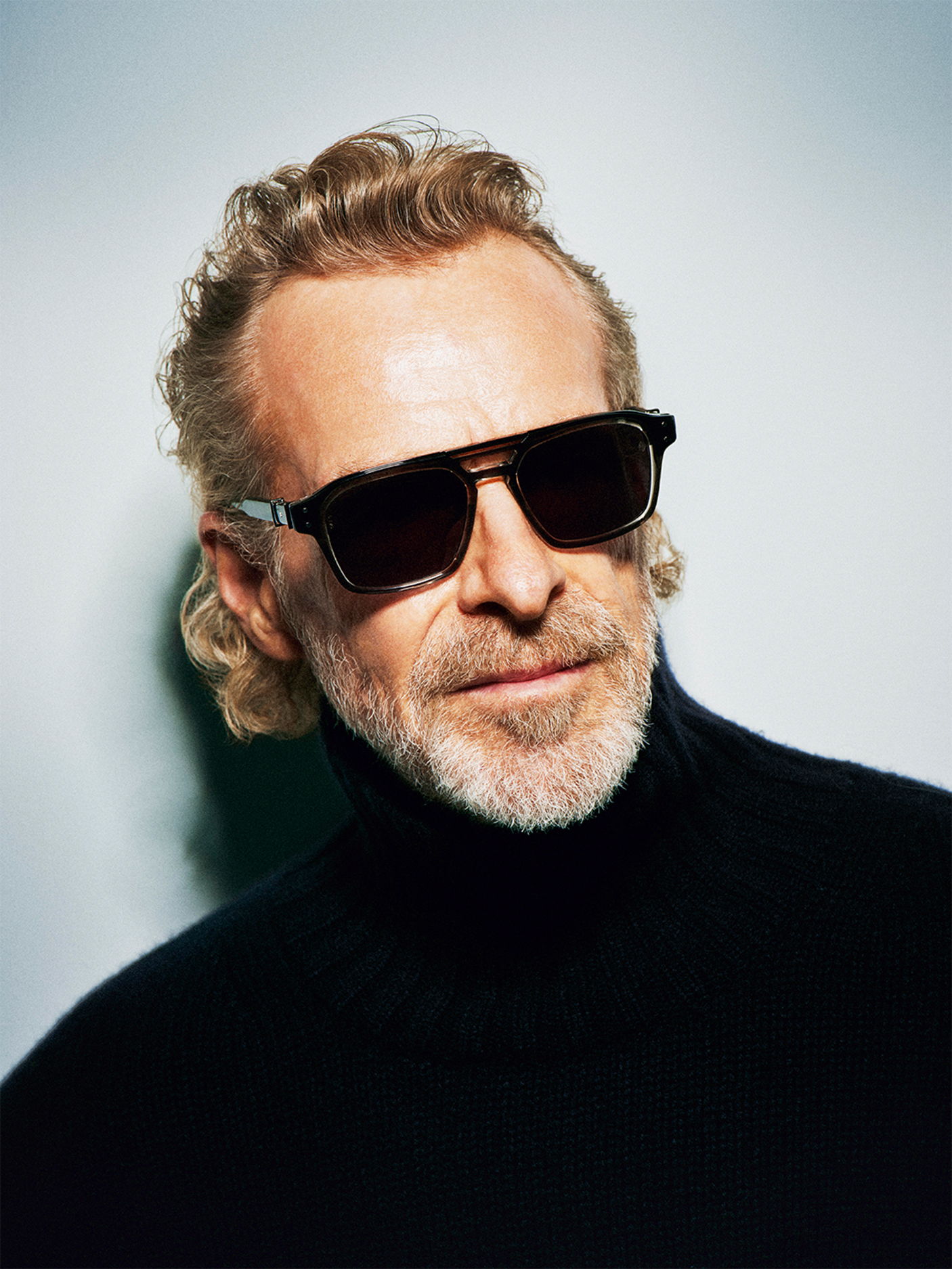 Man wearing Robert Marc sunglasses and a black turtleneck sweater, smiling at the camera.