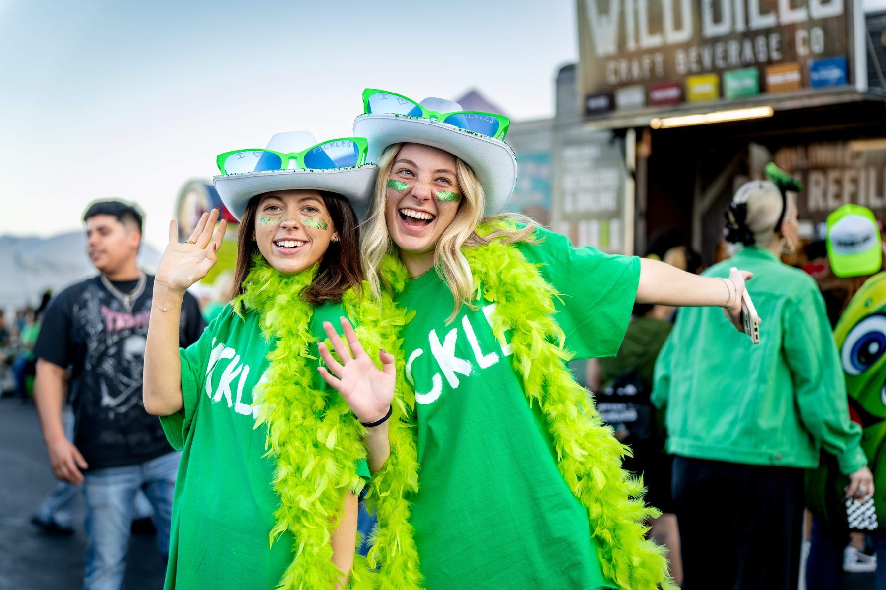 Two guests in matching PICKLES shirts and green feather boas with I love pickles hats at The Big Dill Arlington Texas 2025.