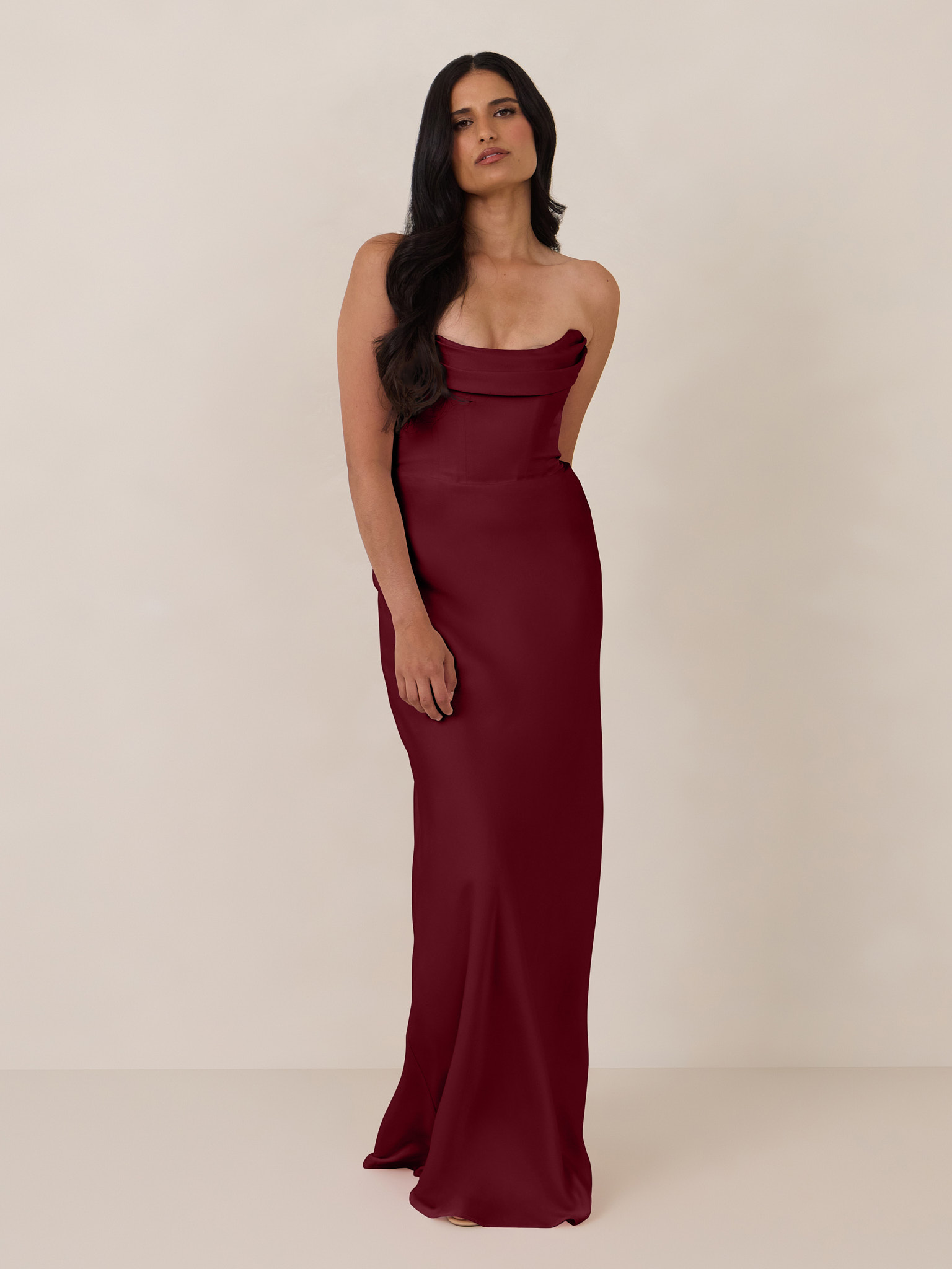 A woman in a burgundy strapless dress standing against a neutral background.