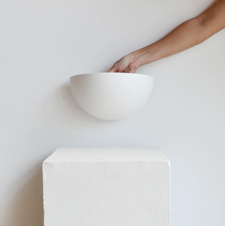 A hand supporting a plaster wall light above a plinth