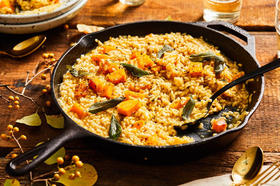 Risotto mixed with sage and butternut squash prepared in a cast iron skillet