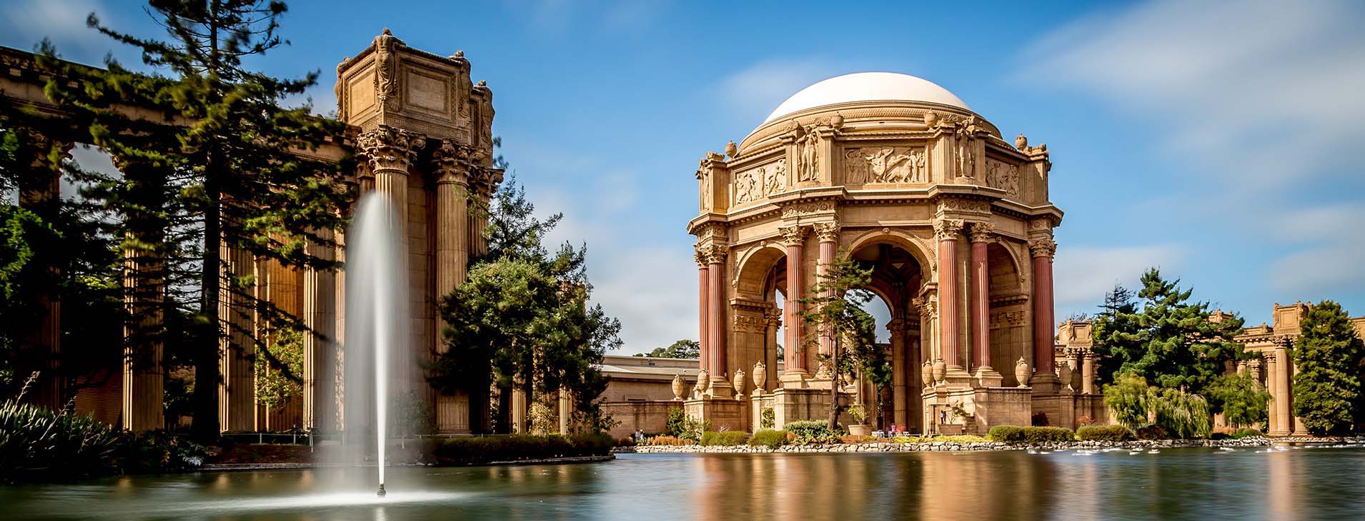 The Palace of Fine Arts in San Francisco, a sprawling Beaux-Arts style complex with trees and water in the landscaping.
