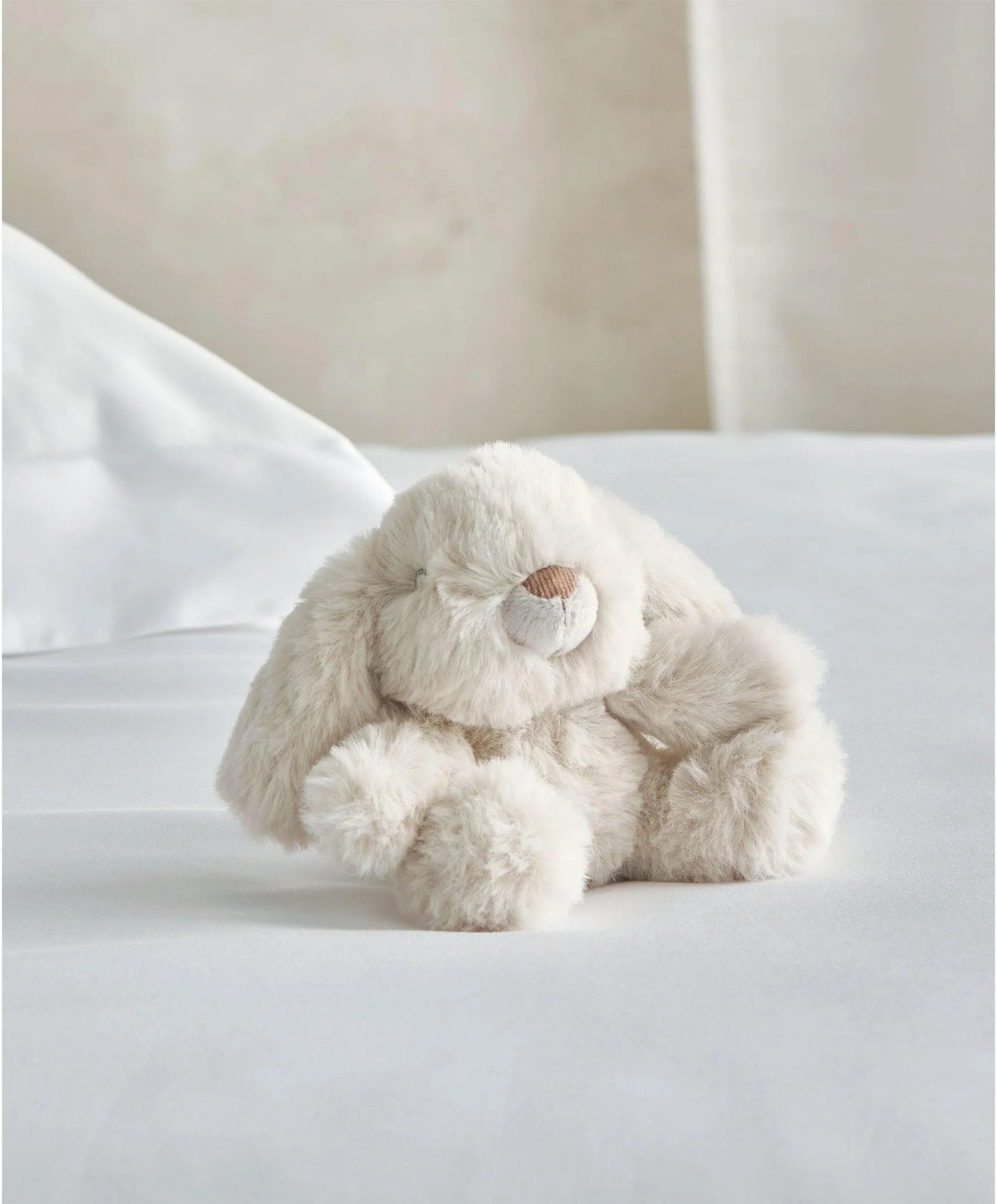 A soft, plush bunny toy sitting on a bed.