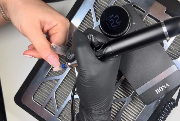 A person using a black electronic device on a nail.