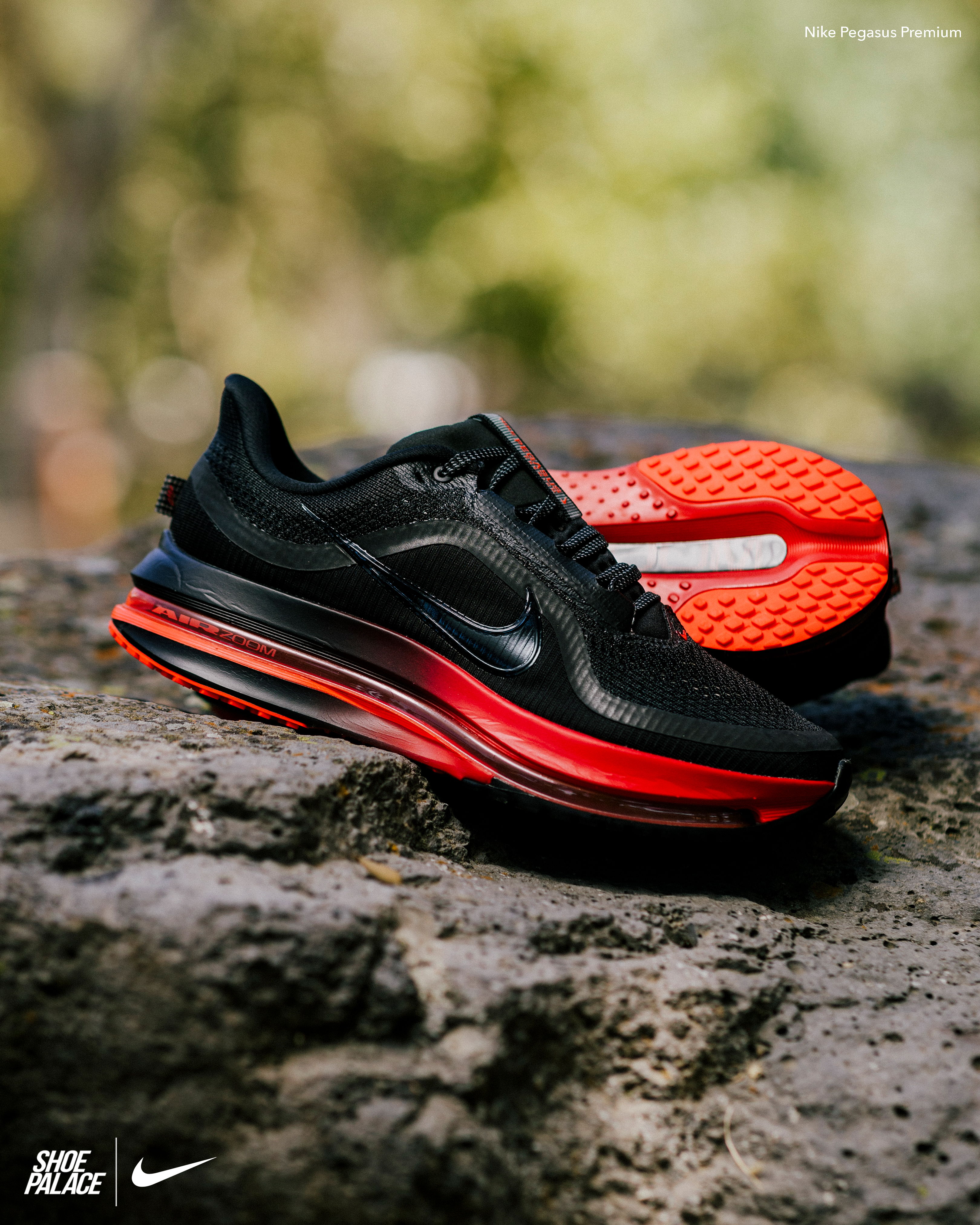 Black and red Nike sneakers displayed on a rocky surface outdoors.