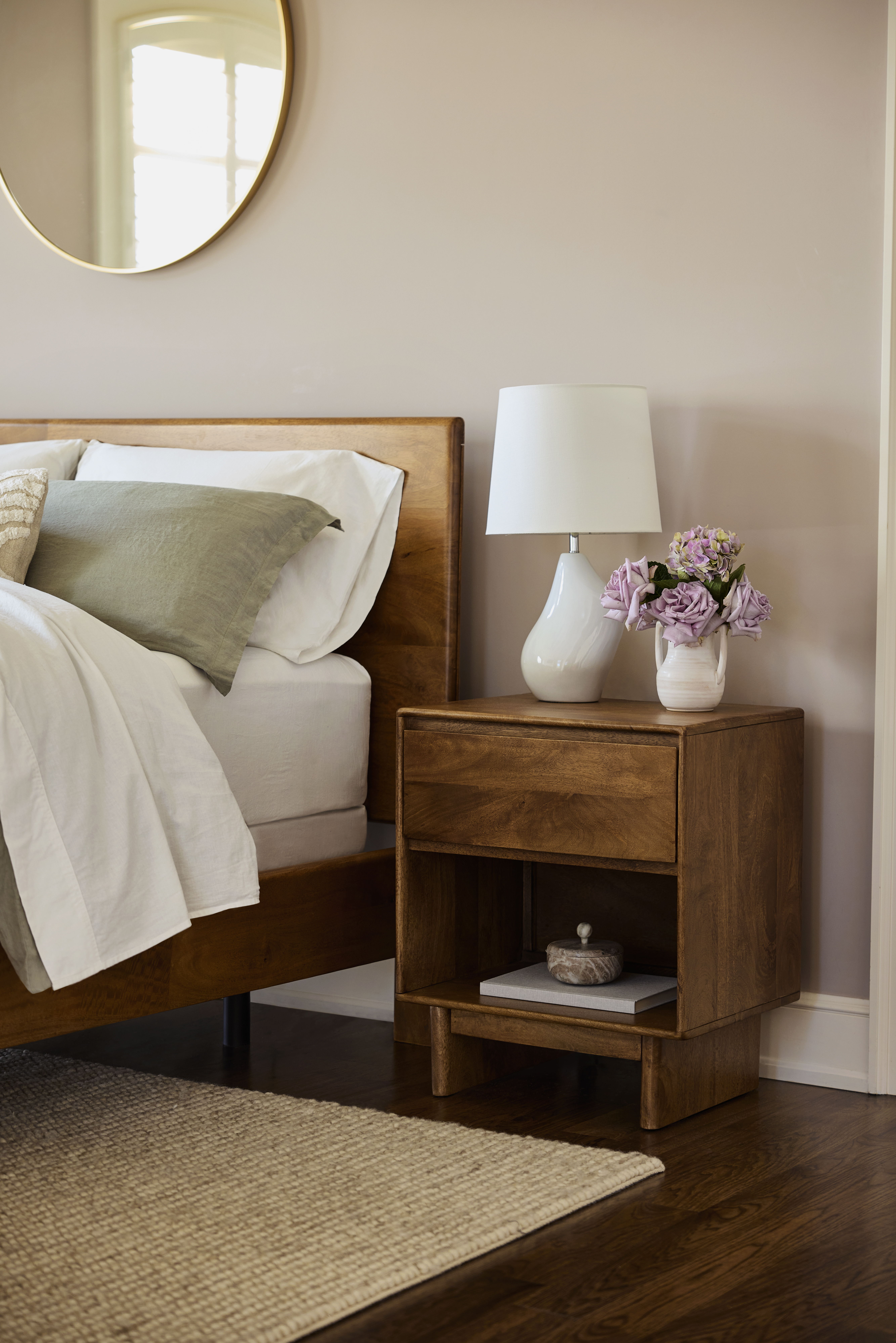 A cozy bedroom with a wooden bed, nightstand, lamp, and flowers.